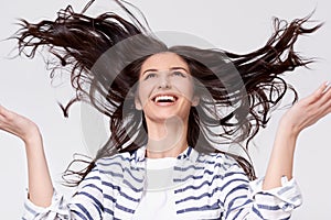 Studio portrait of beautiful joyful brunette woman with flying hair smiling and laughing looking up with raised hands