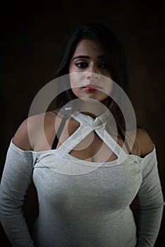 Studio portrait of a beautiful and young Indian Bengali female model in white cold shoulder top and jeans hot pant.
