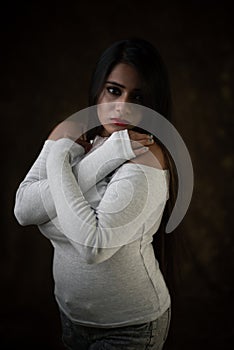 Studio portrait of a beautiful and young Indian Bengali female model in white cold shoulder top and jeans hot pant.