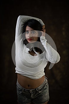 Studio portrait of a beautiful and young Indian Bengali female model in white cold shoulder top and jeans hot pant.