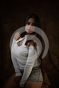 Studio portrait of a beautiful and young Indian Bengali female model in white cold shoulder top and jeans hot pant.