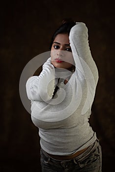 Studio portrait of a beautiful and young Indian Bengali female model in white cold shoulder top and jeans hot pant.