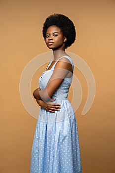 Studio portrait black young woman in blue dress with confident glance arms crossed looking at camera