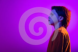 Studio portrait of boy, child looking away with calm expression, posing isolated over purple background in neon light