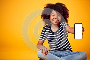 Studio Portrait Of Boy Showing Mobile Phone With Social Media Screen Against Yellow Background