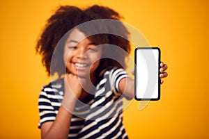 Studio Portrait Of Boy Showing Mobile Phone With Social Media Screen Against Yellow Background