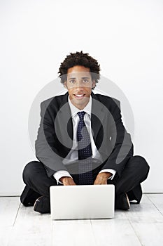 Studio Portrait Of Businessman Sitting On Floor Using Laptop