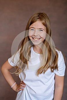 Blonde girl smiles, having with hand in hip on brown background.