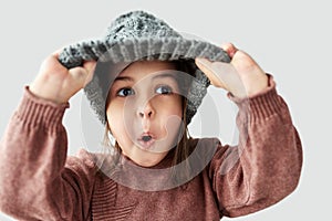 Studio portrait of Caucasian little girl in the winter warm gray hat, has surprised face and wearing sweater isolated on a white