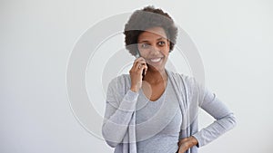 Studio portrait of cheerful black young woman having online conversation using mobile phone standing on white isolated