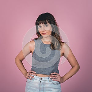 Studio portrait of a confidence woman with hands on hips while looking at camera over a pink background