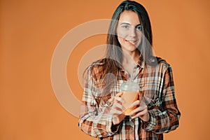 Cute caucasian young brunette girl holding plastic cup of orange juice on orange background