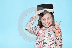 Studio portrait of cute young caucasian girl wearing virtual reality glasses against pastel blue background. Future gadgets.