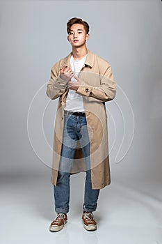 A studio portrait of an East Asian man posing in a coat