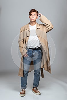 A studio portrait of an East Asian man posing in a coat