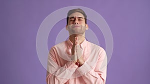Studio portrait of excited young man holding hands folded in prayer beg about something make wish keep fingers crossed