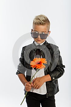 Studio portrait of fashionable blond caucasian boy with single gerbera flower, white background, copy space
