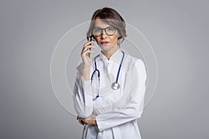 Studio portrait of female doctor wearing labcoat and using mobile phone