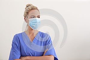 Studio Portrait Of Female Nurse Wearing Scrubs And PPE Face Mask Against White Background