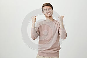 Studio portrait of funny emotive handsome man clasping raised fists and being excited because of victory or successful
