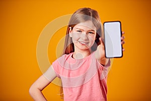 Studio Portrait Of Girl Showing Mobile Phone With Social Media Screen Against Yellow Background