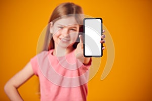 Studio Portrait Of Girl Showing Mobile Phone With Social Media Screen Against Yellow Background