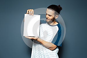 Studio portrait of guy holding white empty paper board on background of blue color
