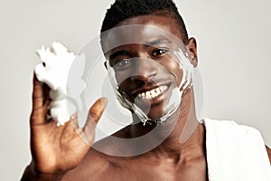 Studio portrait of handsome black guy with naked torso applying cream on his face. Afro American man with towel on his