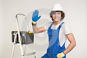 Studio portrait of handsome builder in white helmet and blue overall shaking his hand and laughing.