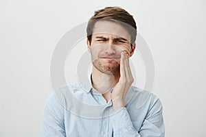 Studio portrait of handsome charming guy with cute smile, raising hands and looking up with excitement, standing against