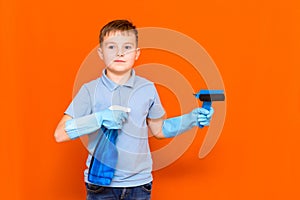 Studio portrait of handsome kid child in gloves cleaning glass with window dehumidifier sprayer. Orange wall