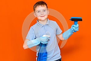 Studio portrait of handsome kid child in gloves cleaning glass with window dehumidifier sprayer. Orange wall