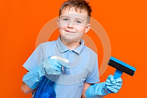 Studio portrait of handsome kid child in gloves cleaning glass with window dehumidifier sprayer. Orange wall