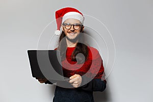 Studio portrait of handsome smiling guy, holding laptop in hands. Wearing Santa Claus hat. Christmas concept. White background