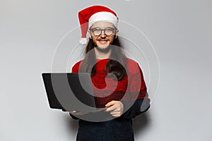 Studio portrait of handsome smiling guy, holding laptop in hands. Wearing Santa Claus hat and eyeglasses. Christmas concept. White