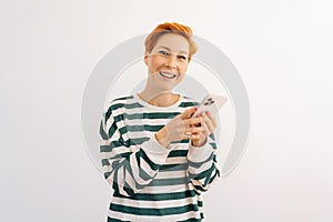 Studio portrait of happy attractive young woman wearing casual clothes standing using mobile cell phone typing sms