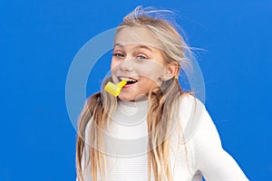 Studio portrait of a happy, smiling young girl celebrating birthday party, holding party blower in mouth having fun