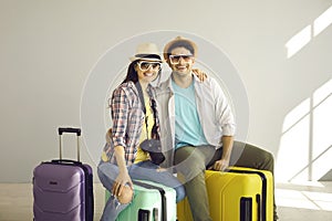 Studio portrait of happy young couple sitting on suitcases packed for holiday trip