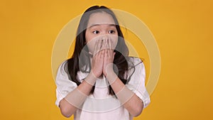 Studio portrait of little asian girl feeling amazement, covering her opened in shock mouth with hands