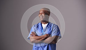 Studio Portrait Of Male Nurse Wearing Scrubs Standing Against Grey Background