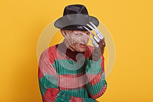 Studio portrait of man in monster makeup, having long hose and ugly face, freak hiding behind his hand, has knives instead of