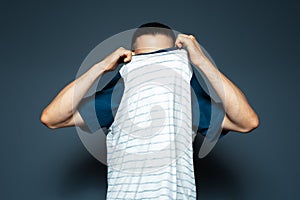 Studio portrait of man undressing the shirt on blue background.