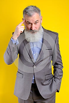 Studio portrait mature businessman dressed in gray suit pointing to head with forefinger, great idea or thought concept