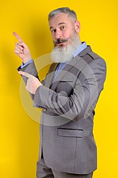 Studio portrait mature businessman dressed in gray suit points aside, I choose you this, yellow background