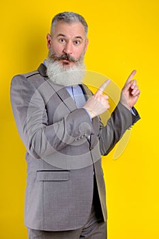 Studio portrait mature businessman dressed in gray suit points aside, I choose you this, yellow background
