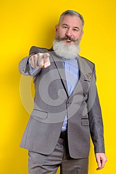 Studio portrait mature businessman dressed in gray suit points to camera, I choose you concept, yellow background