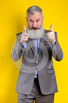 Studio portrait mature businessman dressed in gray suit points to camera, I choose you concept, yellow background