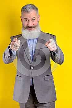 Studio portrait mature businessman dressed in gray suit points to camera, I choose you concept, yellow background