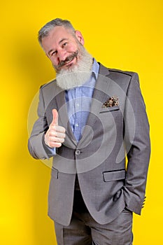 Studio portrait mature businessman dressed in gray suit shows thumb up, successful business concept, yellow background