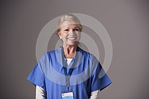 Studio Portrait Of Mature Female Nurse Wearing Scrubs Standing Against Grey Background